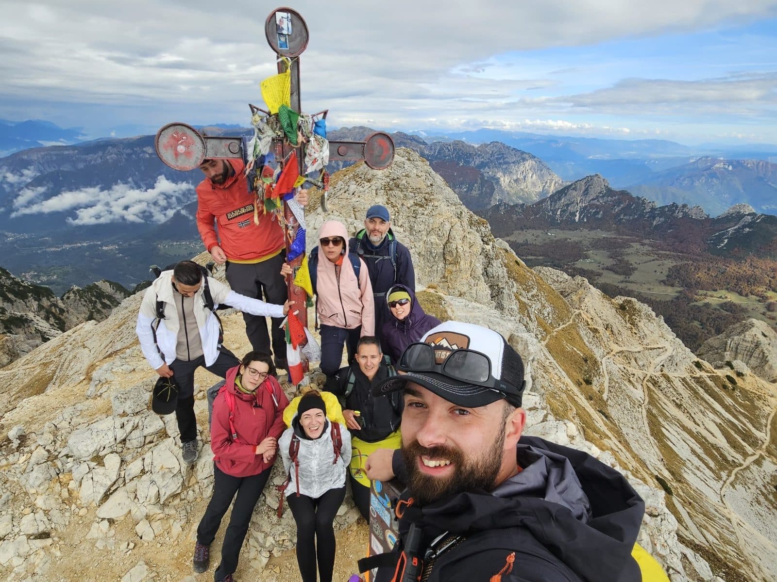 Group selfie at the summit cross of Cima Carega, with the valleys behind