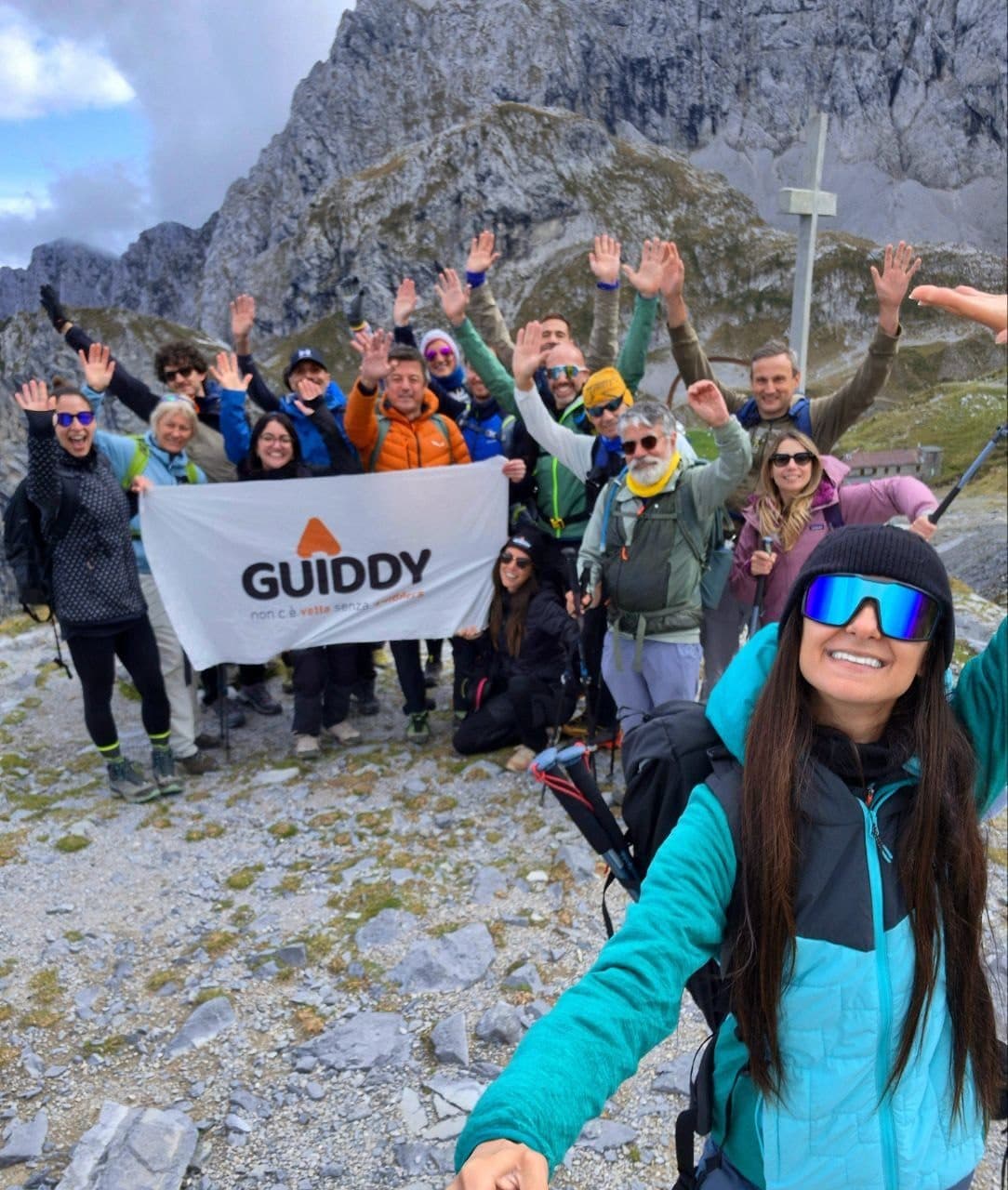 Group selfie with arms raised and the Guiddy flag below the Presolana