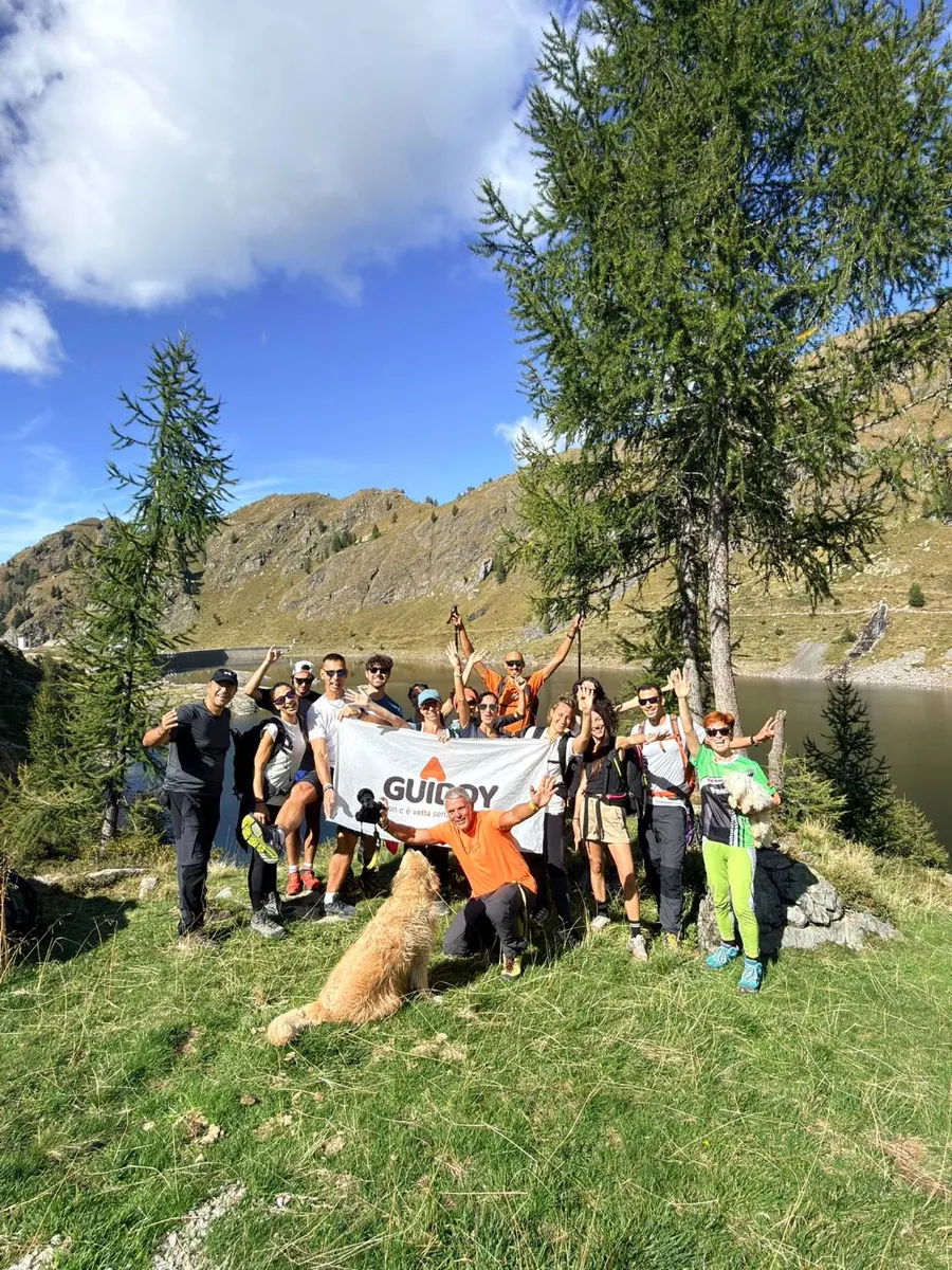Un gruppo di Guidders a braccia alzate con la bandiera Guiddy in riva a un lago di montagna