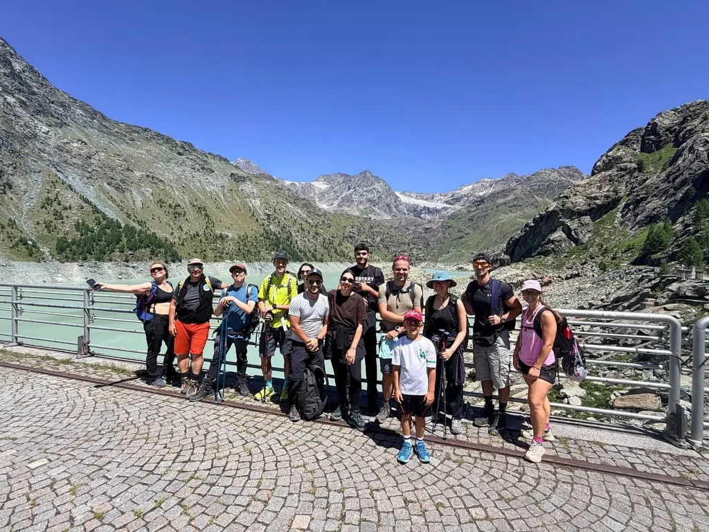 Un gruppo di Guidders sorridenti in fila sulla diga di un lago glaciale, con le montagne alle spalle