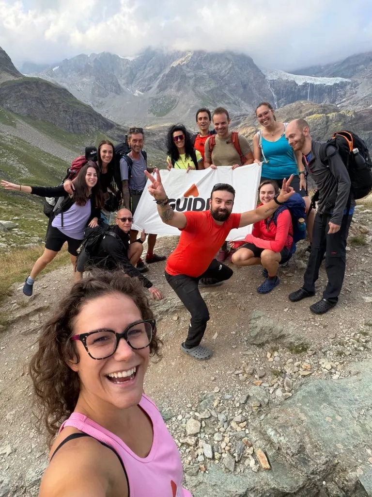 Selfie sorridente di un gruppo di Guidders con la bandiera Guiddy e il ghiacciaio alle spalle