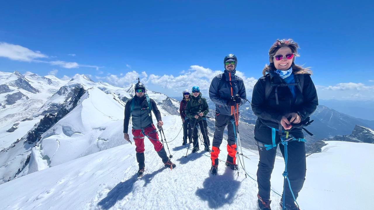 Un gruppo di cinque in vetta, legati, con le Alpi innevate dietro