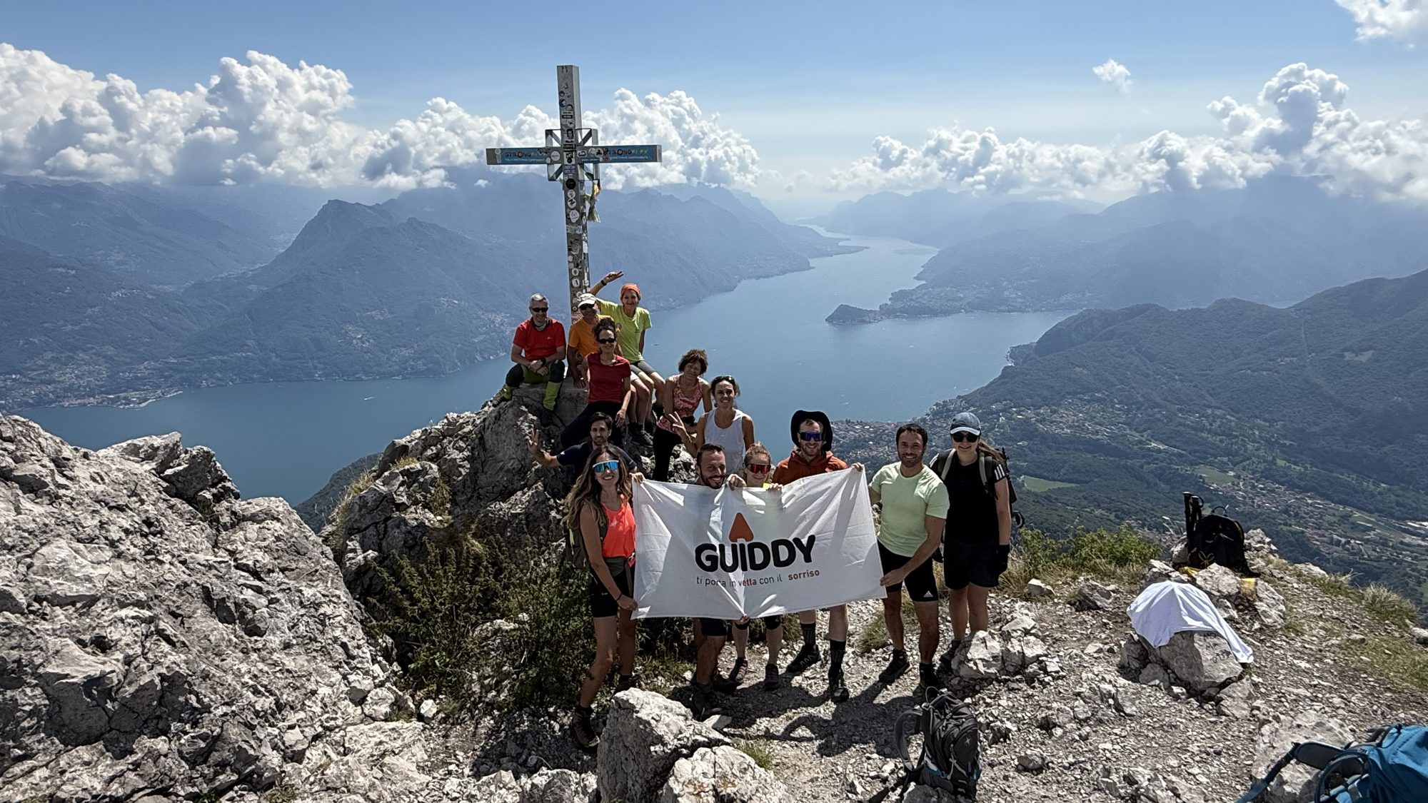 Un gruppo Guiddy in vetta con la bandiera, sotto il lago di Como